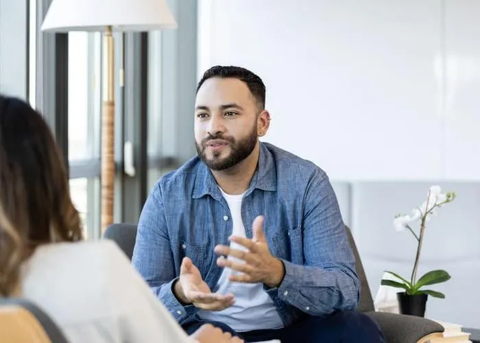 A young male therapy patient gestures as he talks about something with a female therapist.