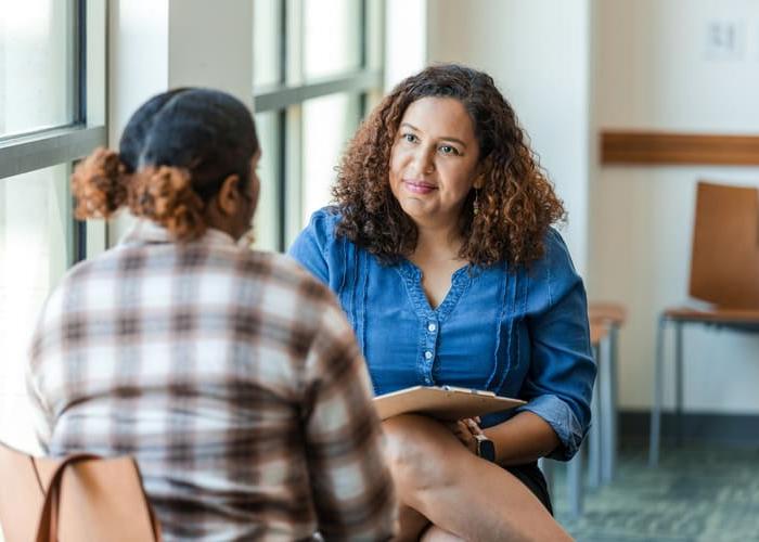 Two women in casual clothing having a discussion. One is a mental health professional, listening intently.