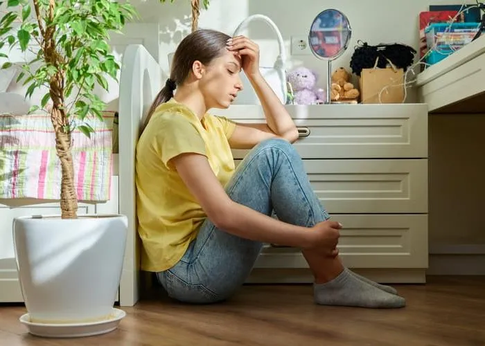 Sad teenage girl sitting on the floor at home. Upset female high school student in room. Teenage problems, stress, depression, adolescence, mental health concept