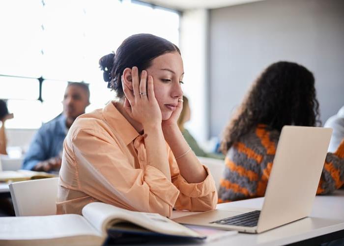 Young female college student sitting at a table and looking distracted during a lesson in a classroom at school