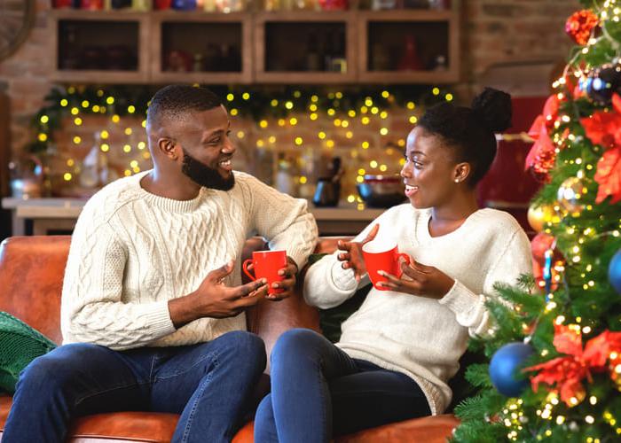 Romantic african american couple celebrating Christmas eve together at home, drinking hot chocolate and chatting